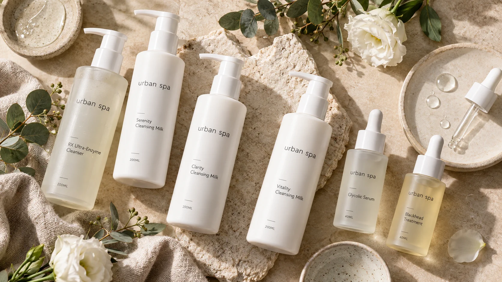 Urban Spa professional skincare range: white pump bottles of RX Ultra-Enzyme Cleanser, Serenity, Clarity and Vitality Cleansing Milk, alongside dropper bottles of Glycolic Serum and Blackhead Treatment